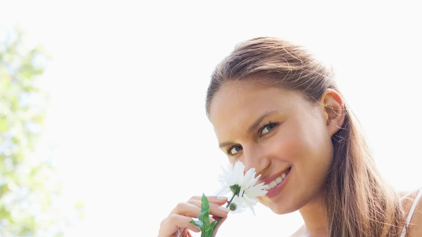 Smiling woman in the park smelling a flower