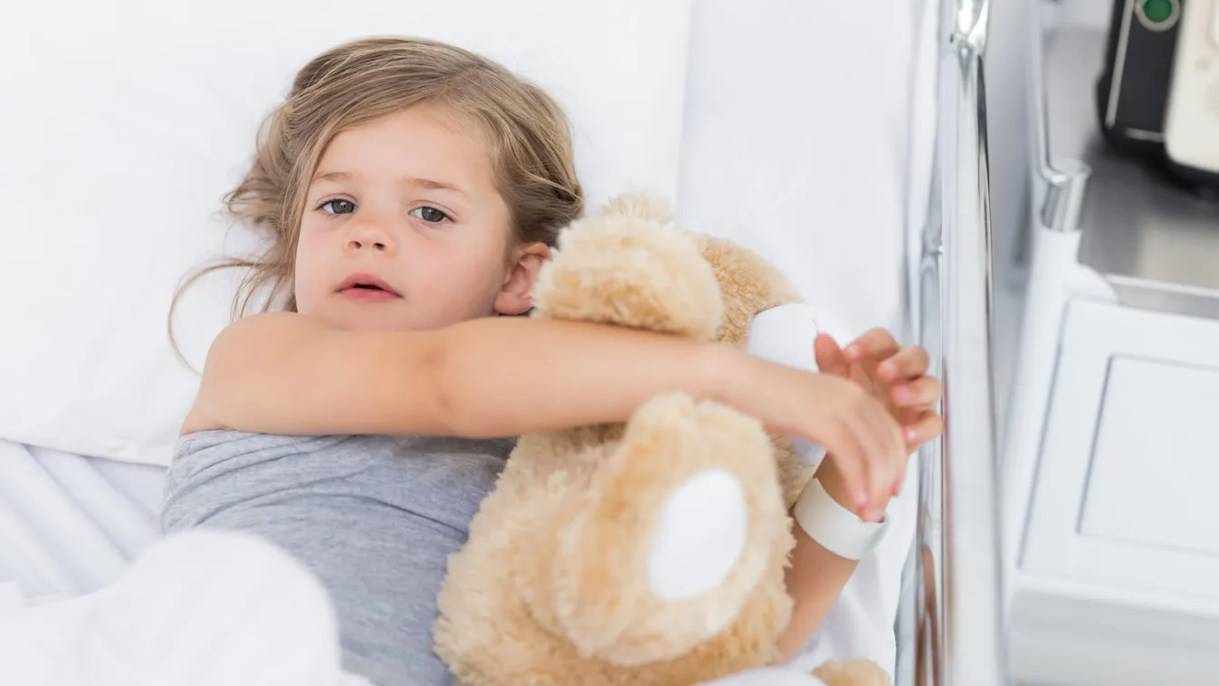 High angle portrait of cute girl hugging teddy bear while lying in hospital bed