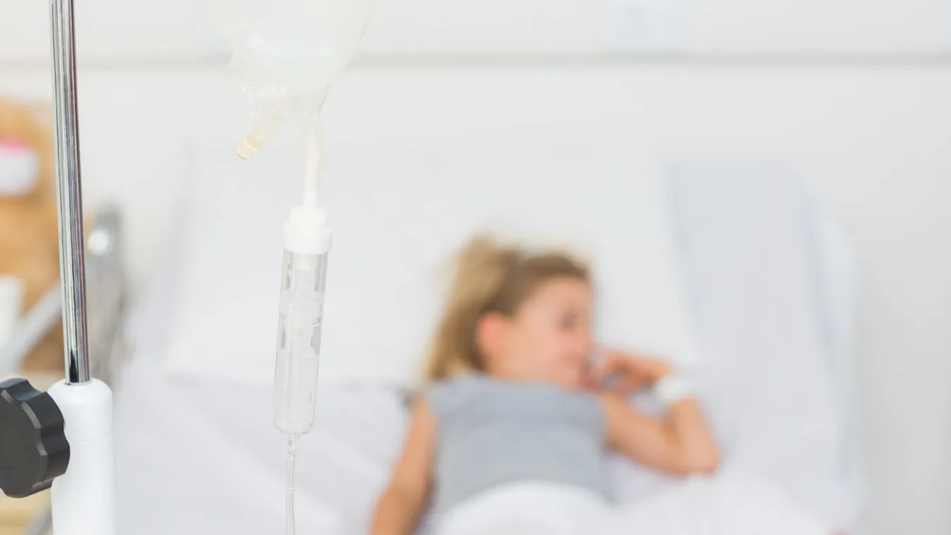 Focus on IV drip with sick little girl in hospital bed