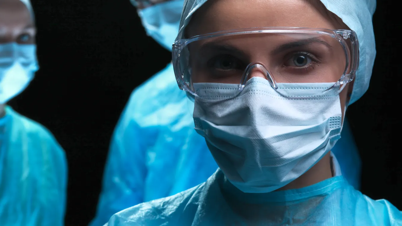 Three surgeons at work operating in surgical theater saving patient and looking at life monitor. Resuscitation medicine team wearing protective masks. Surgery and emergency concept