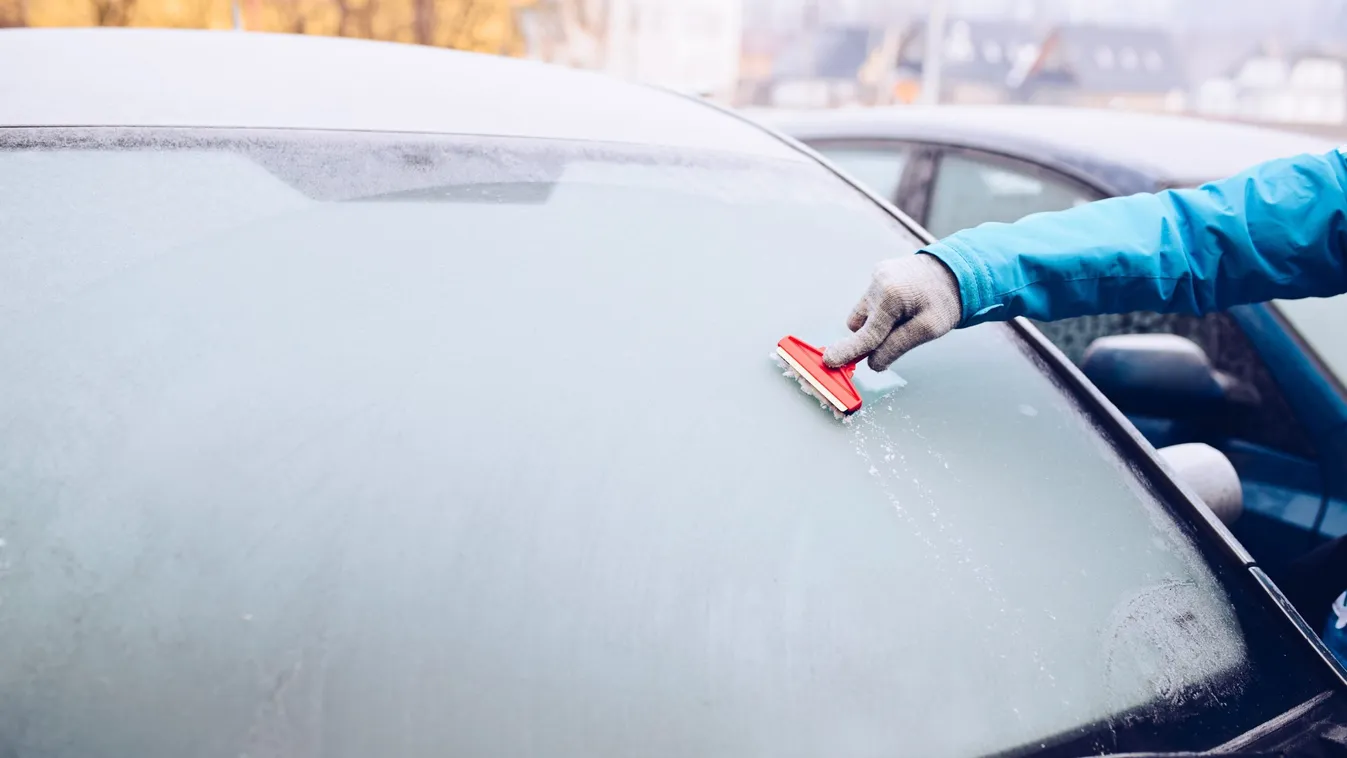 Woman removing ice from car windshield with glass scraper.