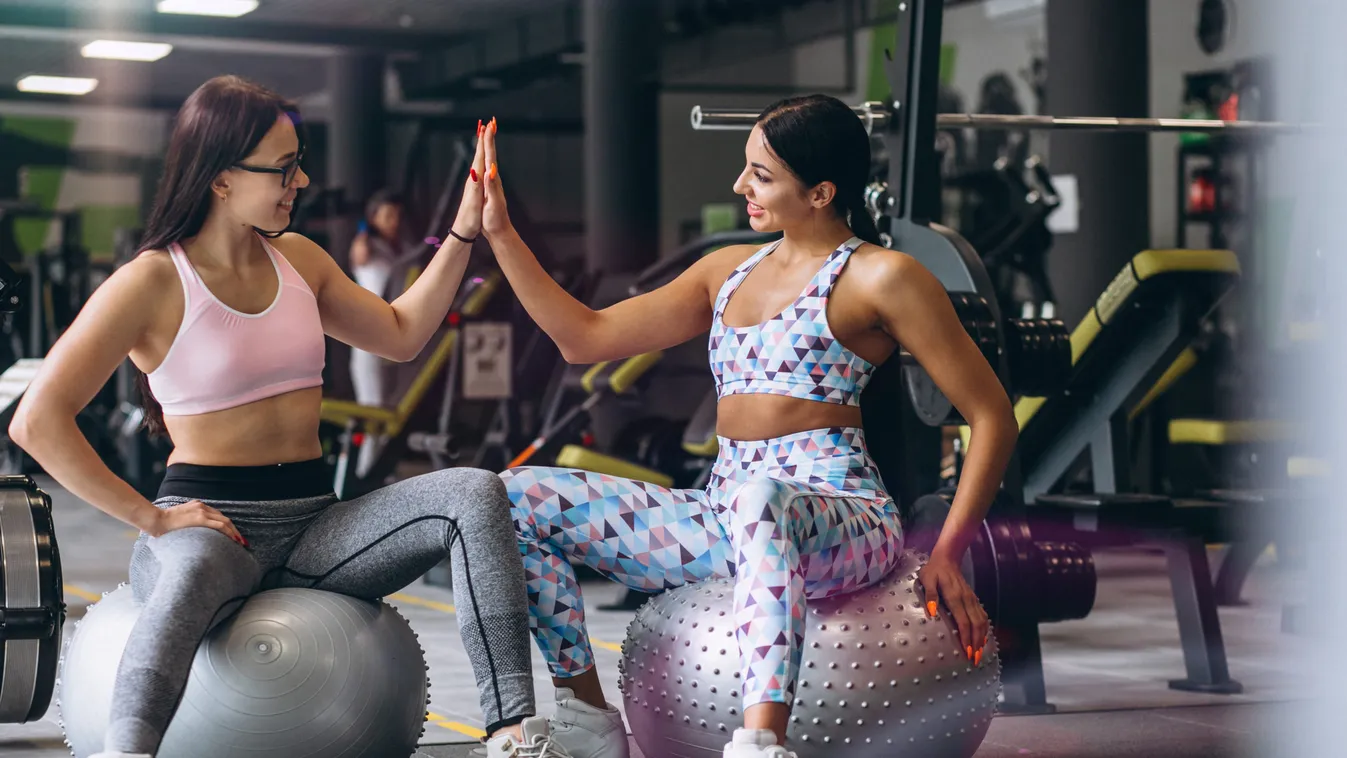 Two young girls training at gym sitting on fitness ball