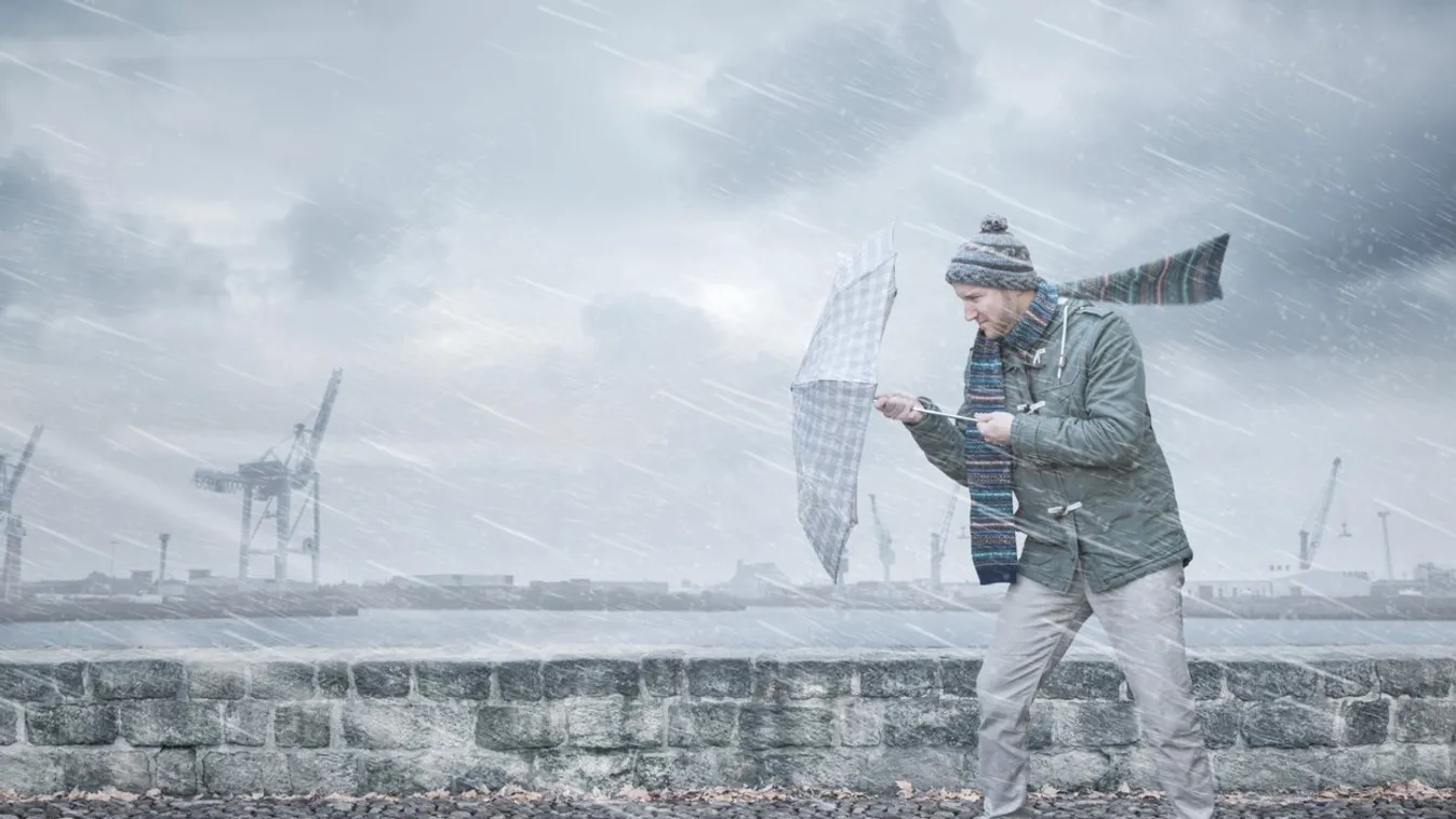 Pedestrian with an umbrella is facing strong wind and rain