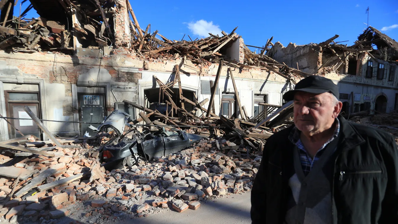 A man stands on a street next to destroyed houses on a street after an earthquake in Petrinja