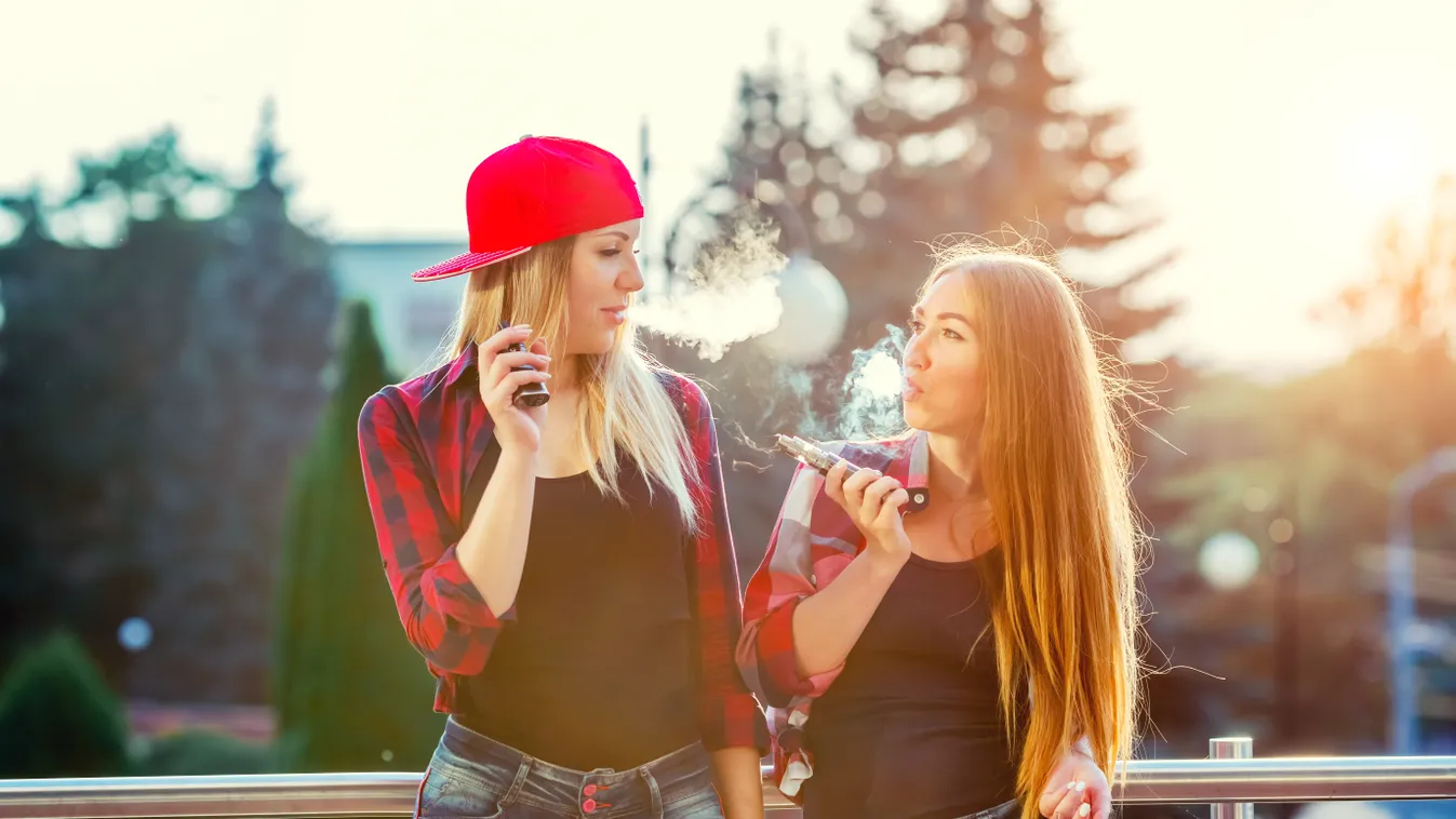 Two women vaping outdoor. The evening sunset over the city. Toned image.