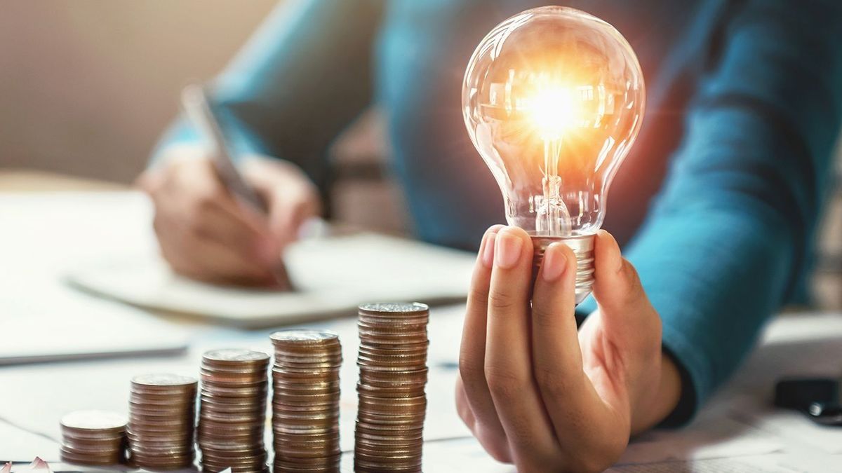 Business,Woman,Hand,Holding,Lightbulb,With,Coins,Stack,On,Desk.