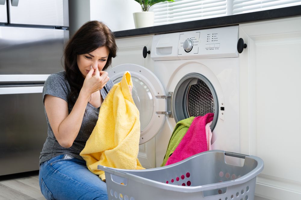 Young,Woman,Looking,At,Smelly,Clothes,Out,Of,Washing,Machine