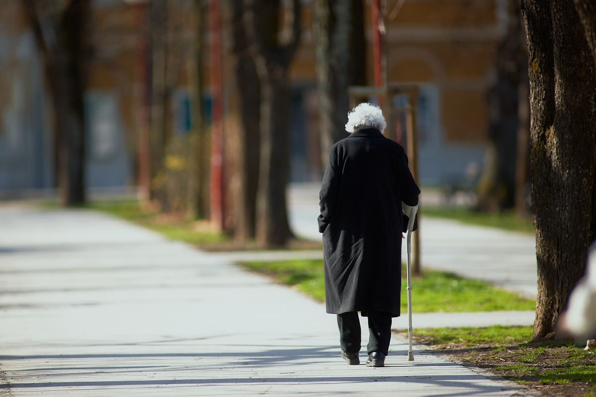 Old,Woman,Walking,Down,The,Street,With,Walking,Stick