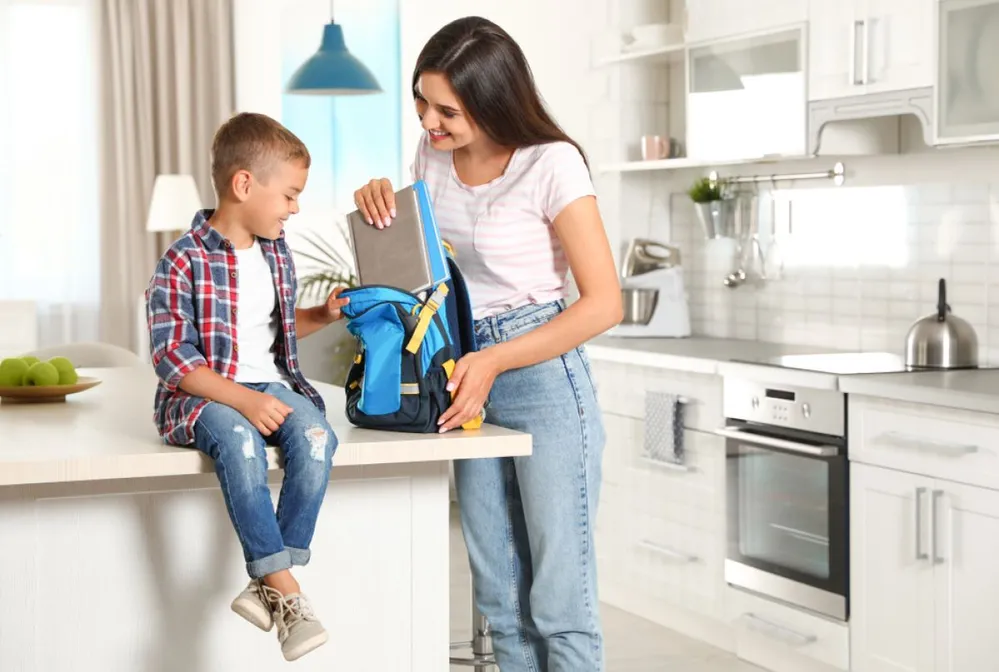 Happy,Mother,Putting,Textbooks,Into,Little,Child's,School,Bag,In