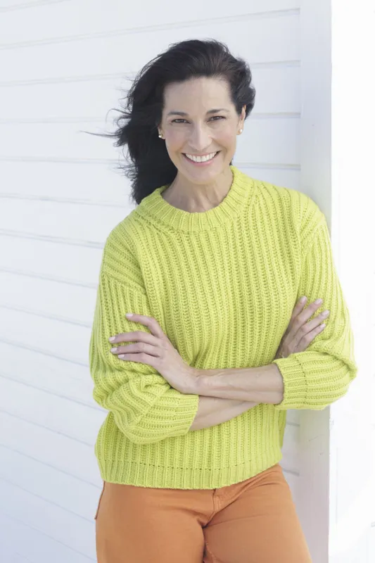 Mature, dark-haired woman in a green and yellow knit sweater and orange pants