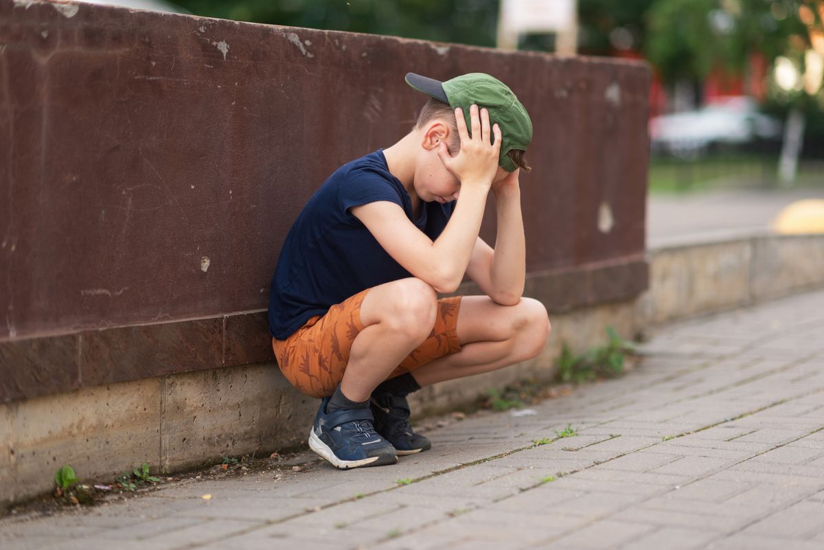 A,Teenage,Boy,Is,Squatting,Leaning,Against,A,Concrete,Wall