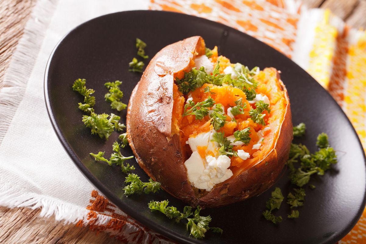 sweet potatoes baked with cream cheese, butter and parsley close-up on a black plate. horizontal