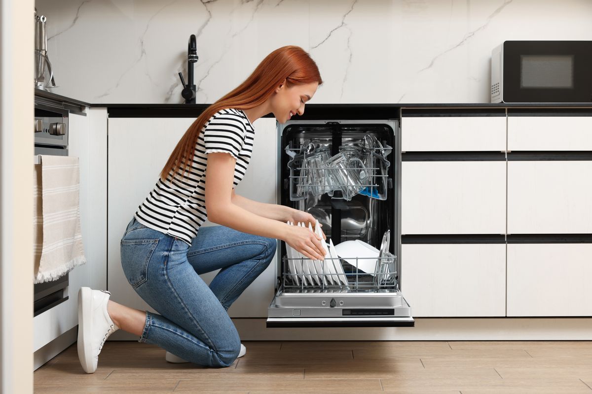 Smiling,Woman,Loading,Dishwasher,With,Plates,In,Kitchen