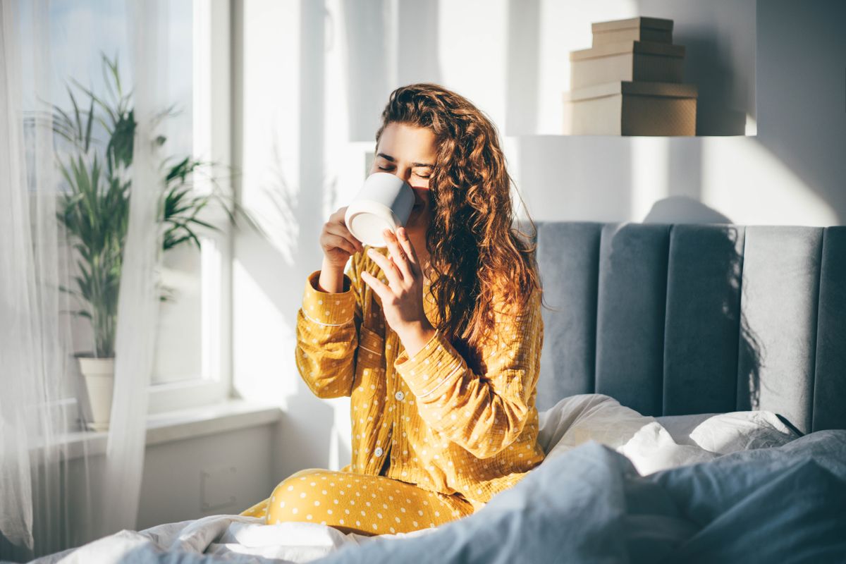 Woman,In,Yellow,Pajama,Sitting,On,Bed,And,Drinking,Coffee