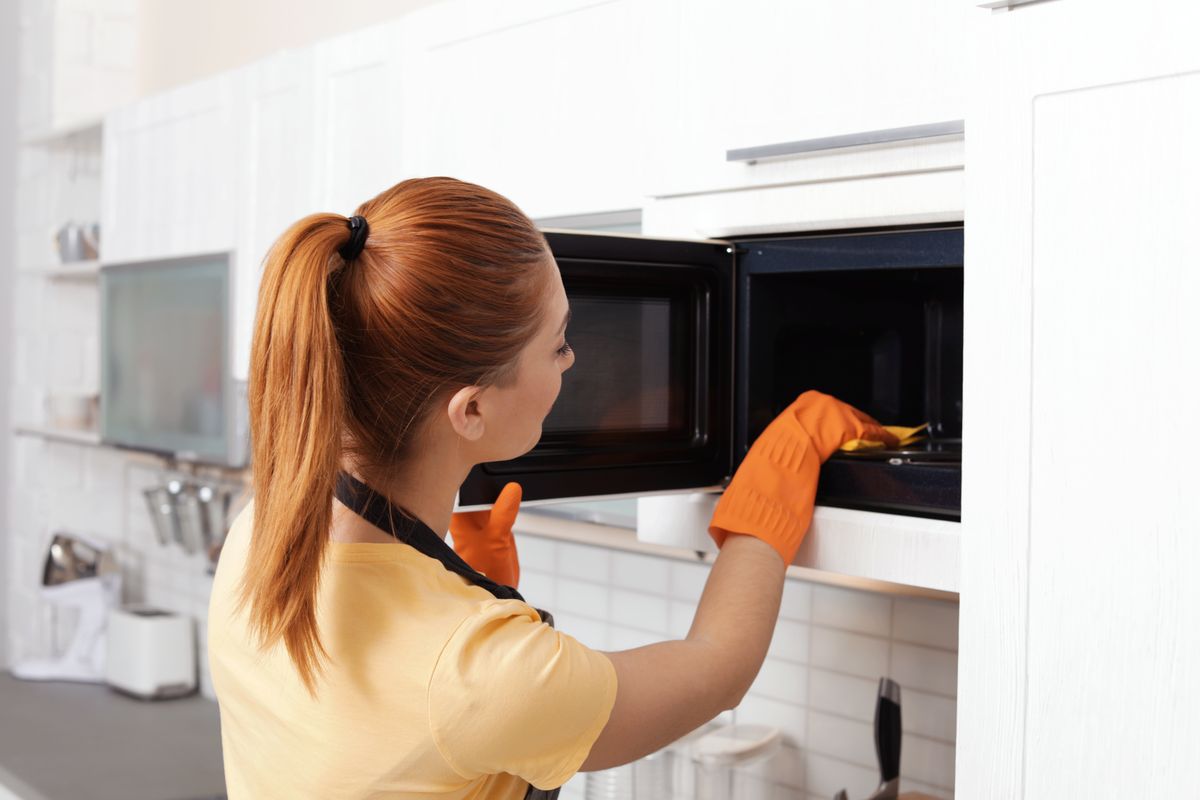 Woman,Cleaning,Microwave,Oven,With,Rag,In,Kitchen