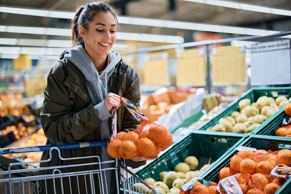 Young,Happy,Woman,Choosing,Oranges,In,Plastic,Mesh,While,Buying