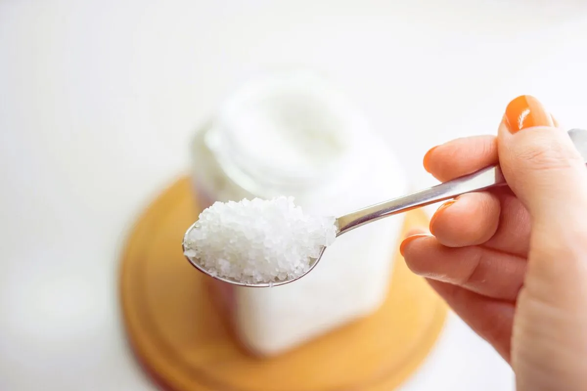 Female,Hand,Holds,A,Spoon,With,White,Sea,Salt.,Blurred
