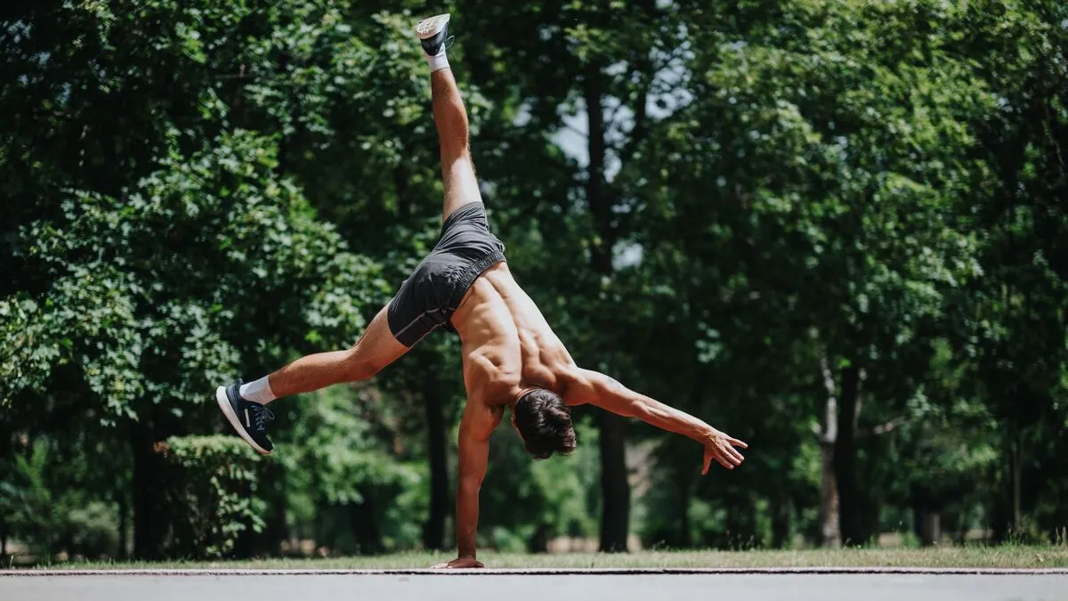 Athletic man performing a one-handed handstand outdoors in a park