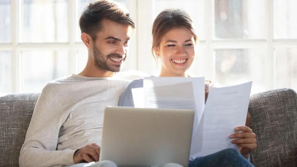 Smiling,Husband,And,Wife,Sit,On,Couch,Using,Laptop,Taking, hitel, szerződés, papír, otthon start, dokumentum,