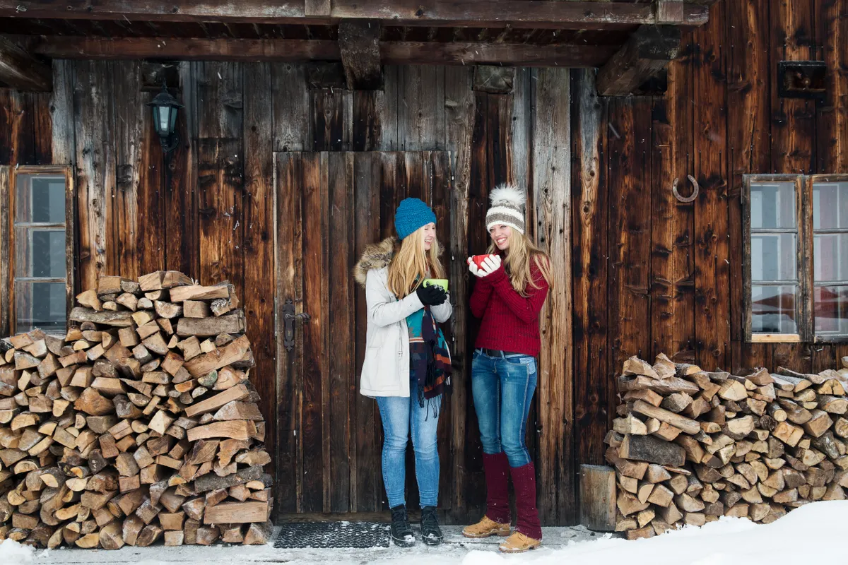 Two young female friends chatting outside wooden cabin