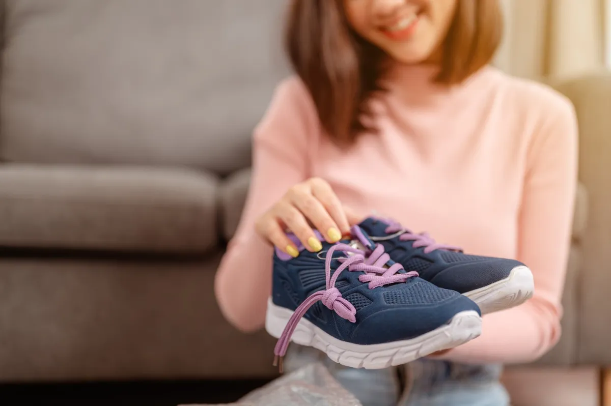 Woman sitting in the living room is excited about opening a new parcel box and shoes from online shopping at home for the holidays.