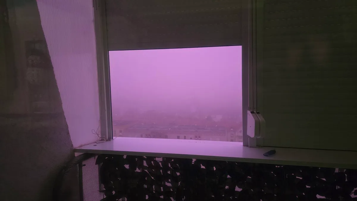 Lila köd borítja be a várost, a fények beömlenek a félig felhúzott redőnyön át.