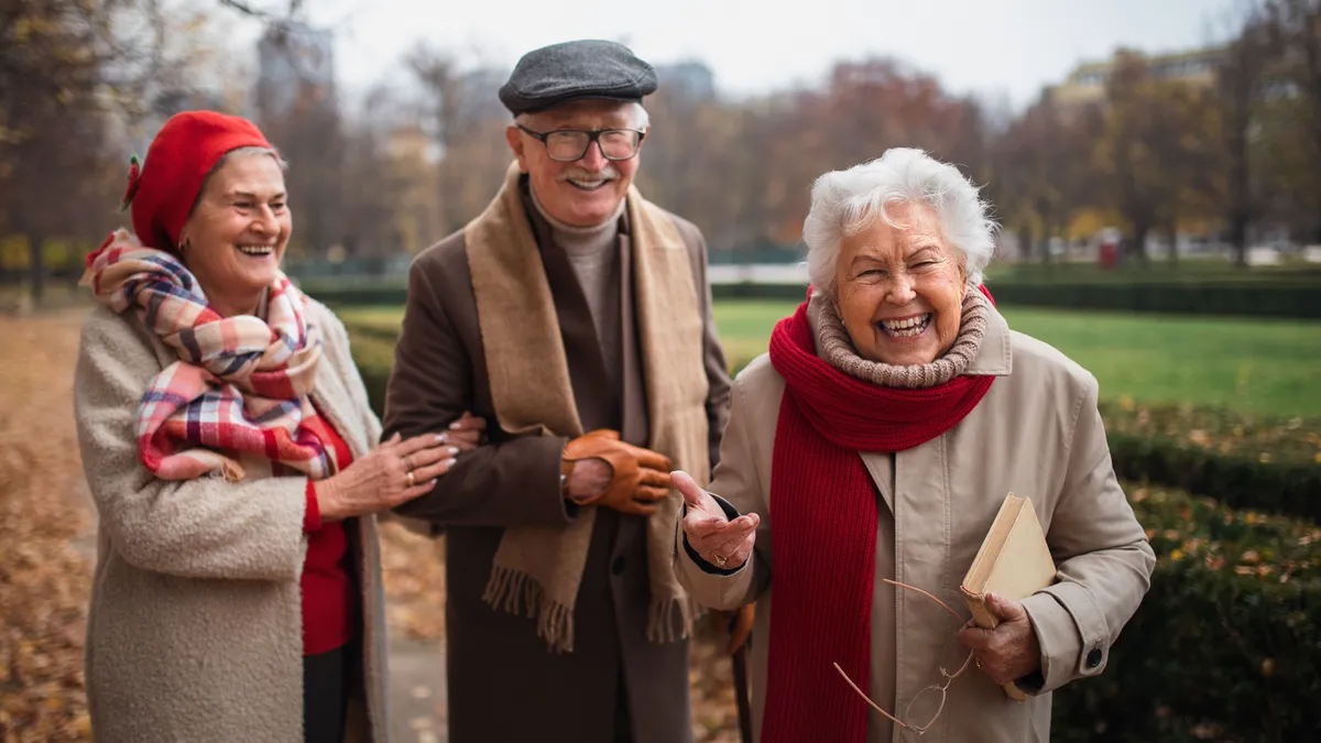 Group of happy senior friends on walk outdoors in town park in autumn, looking at camera.