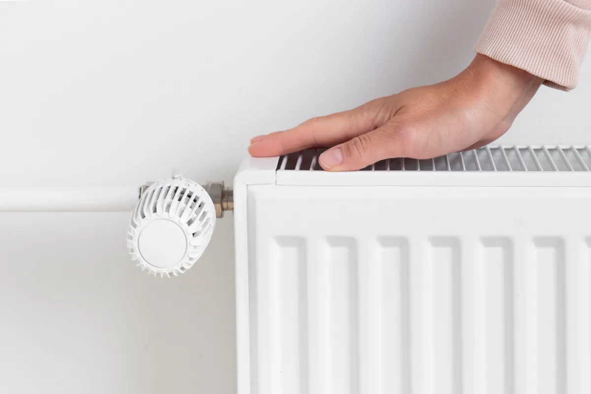 A,Woman,Warming,Her,Hands,On,A,Heating,Radiator,,The
