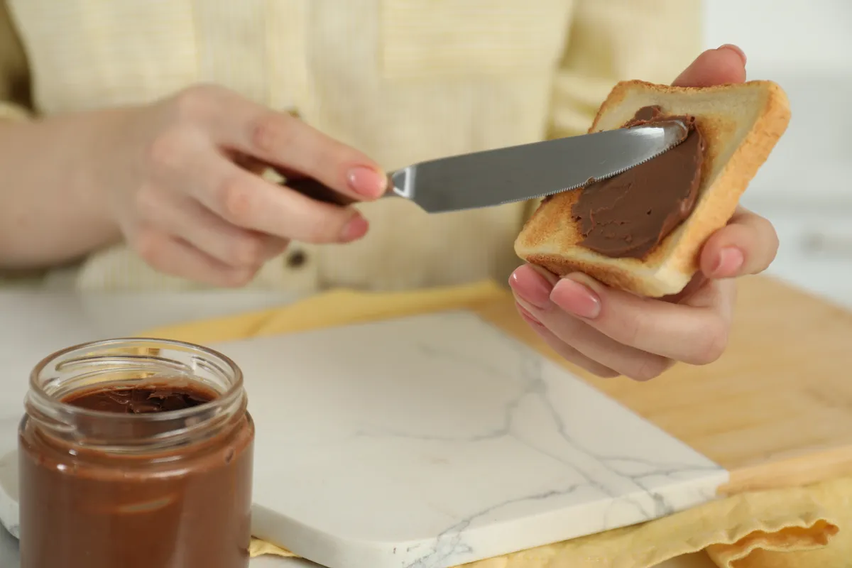 Nutella Woman,Spreading,Tasty,Nut,Butter,Onto,Toast,At,Table,,Closeup